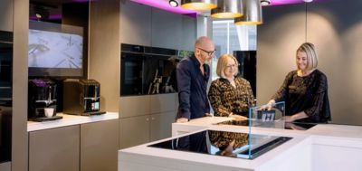 Three individuals are gathered around a kitchen counter, examining its contents and discussing their options.  