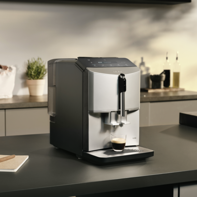 Une machine à café Siemens EQ300 sur un comptoir avec un café sous le distributeur et un bloc-notes avec un stylo à côté.