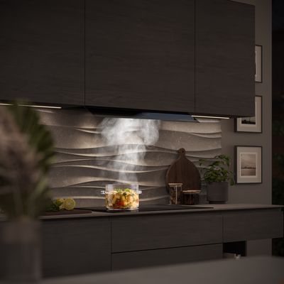 Matzwarte Siemens afzuigkap boven een pan die stoomt met kleurrijke groenten, geplaatst tegen een textuurwand. 