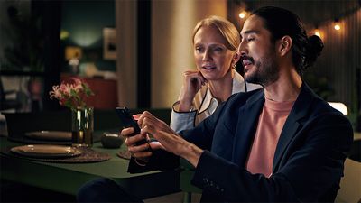 A man and woman are seated at a table, looking intently at a phone together.  
