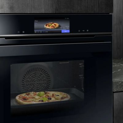 A pizza is cooking inside a microwave oven, with steam visible as it heats up. 