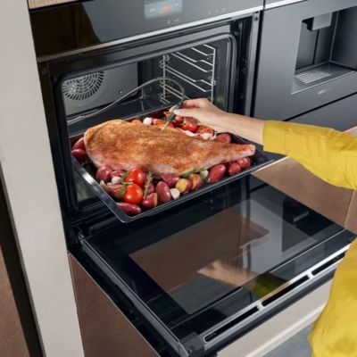 A woman removes a piece of meat from the oven, using a meat probe to check its temperature. 