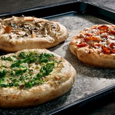 Three pizzas with various toppings arranged on a baking tray, ready for baking. 