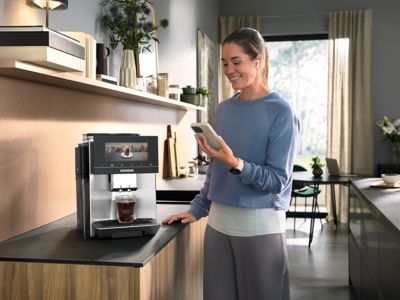 Mädchen nutzt ein Smartphone neben einer Siemens Kaffeemaschine in einer modernen Küche.