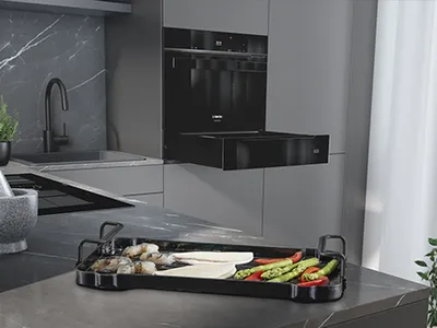 Modern kitchen with a black countertop tray holding assorted vegetables and seafood.