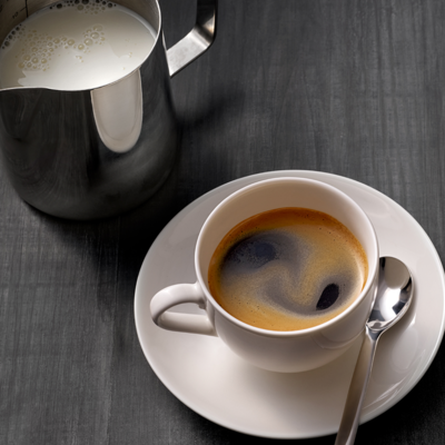 Un americano et un petit pot à lait sont posés sur une table en bois brun-noir.
