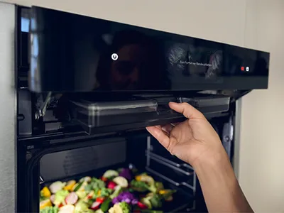 Eine Hand öffnet einen NEFF Ofen mit Dampfunterstützung, gefüllt mit buntem Gemüse.