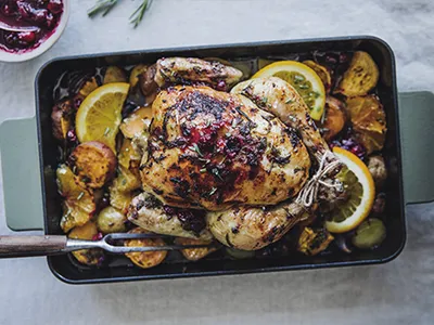 Goldbraunes Brathähnchen mit Zitronenscheiben und Gemüse in einer schwarzen Backform.