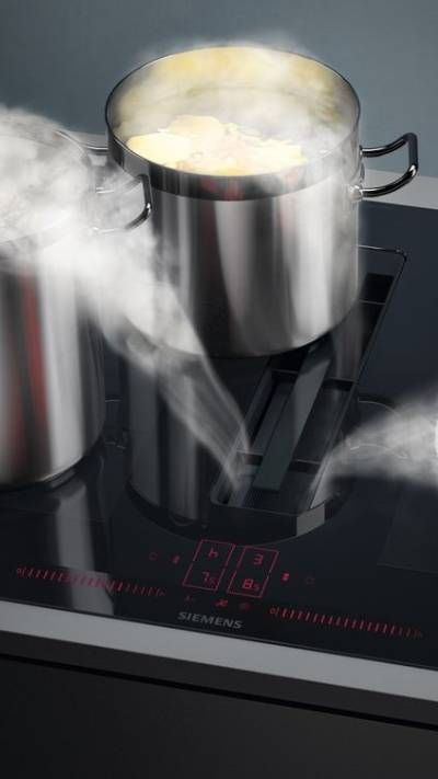 Placa de inducción Siemens con ollas y sartenes humeantes, mostrando un proceso de cocción en una cocina moderna.