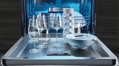 Interno di una lavastoviglie Siemens da incasso con luce led blu e una serie di stoviglie di ceramica bianca appoggiate sullo sportello.