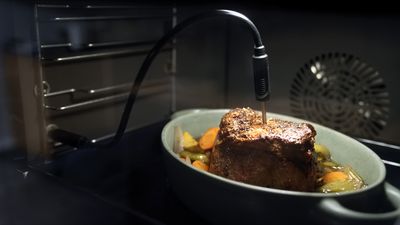 A meat probe inserted into a roasting joint with vegetables in an oven, ensuring precise cooking.