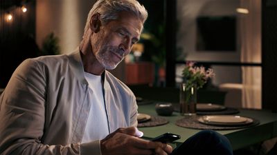 Ein älterer Mann sitzt am Küchentisch und bedient sein Smartphone.