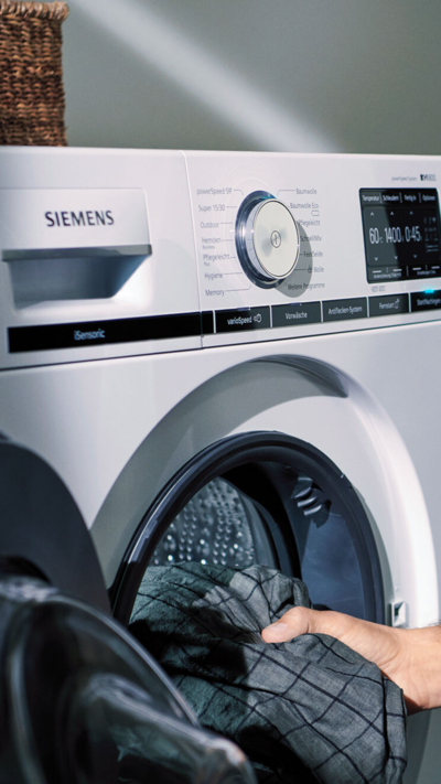 ein Mann zieht sich ein Hemd an, hinter ihm stehen ein Trockner und Waschtrockner von Siemens