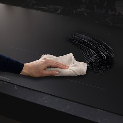 Een hand veegt een  zwart aanrecht schoon met een doek.