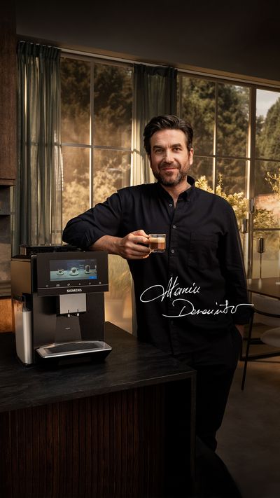 Mężczyzna trzymający filiżankę kawy obok ekspresu do kawy Siemens w eleganckiej  kuchni z dużymi oknami