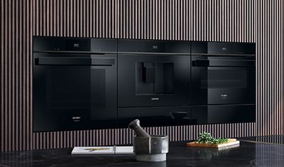 A row of integrated black Siemens kitchen appliances, including an oven, coffee machine, and microwave, set against a modern wooden slatted wall.