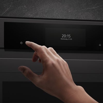  Close-up van een hand die de aan/uit-knop op een  digitaal ovenbedieningspaneel indrukt dat de tijd en datum weergeeft.