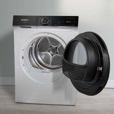 Une personne met une chemise foncée dans un sèche-linge Siemens au design élégant, dans une buanderie cosy. 
