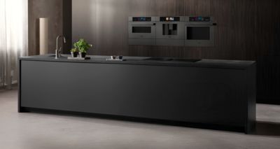 Questa cucina moderna &egrave; caratterizzata da una raffinata isola di colore nero, con un elegante rubinetto e forni Siemens integrati in una parete in legno scuro ravvivata dalle tonalit&agrave; di verde delle piante decorative.