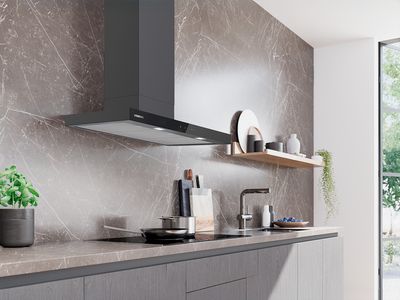 Cucina moderna con cappa inox sopra piano cottura, vapore sale da pentola su piano elegante con mobili in legno. 