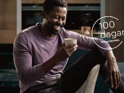 En person i en lavendelfärgad långärmad skjorta håller en kopp, sittande bekvämt i ett modernt kök.