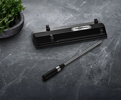 Un elegante electrodom&eacute;stico negro de Siemens con una sonda de cocci&oacute;n sobre una superficie gris texturizada, junto a una peque&ntilde;a planta en maceta.