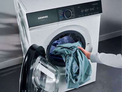 A person holds a smartphone displaying a washing machine app interface in a modern kitchen.