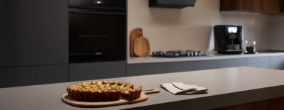 Uma tarte acabada de cozer numa t&aacute;bua de madeira, elegantemente exposta numa cozinha Siemens moderna, exibindo excel&ecirc;ncia culin&aacute;ria.