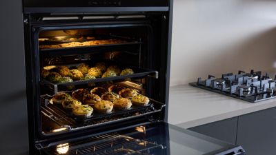 Forno Siemens cheio de uma variedade de muffins e bolachas coloridos, exibindo criatividade culin&aacute;ria numa cozinha moderna.