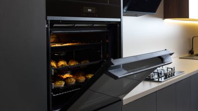 Forno Siemens com a porta aberta, revelando deliciosos muffins a cozer na perfei&ccedil;&atilde;o numa cozinha moderna. Efici&ecirc;ncia encontra estilo.