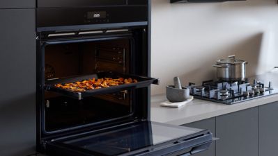 Forno Siemens com um tabuleiro de vegetais assados coloridos, real&ccedil;ando uma cozinha contempor&acirc;nea com funcionalidade e estilo.
