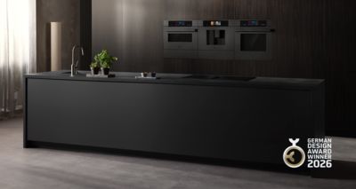       &Icirc;lot de cuisine noir moderne avec des appareils &eacute;l&eacute;gants, un robinet et des herbes en pot, affichant le logo du German Design Award Winner 2026.     