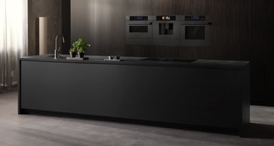 Tato modern&iacute; kuchyně představuje elegantn&iacute; čern&yacute; ostrůvek, stylovou baterii a vestavn&eacute; trouby Siemens na pozad&iacute; tmav&eacute; dřevěn&eacute; stěny, zat&iacute;mco sytě zelen&eacute; rostliny dod&aacute;vaj&iacute; svěž&iacute; n&aacute;dech.