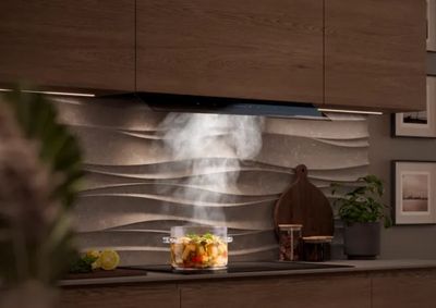 Een moderne keuken met warme houten kastjes, een stoere gestructureerde achterwand en een dampende pan op een kookplaat onder een stijlvolle Siemens afzuigkap.