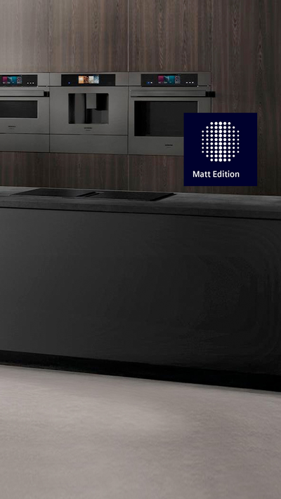 Diese moderne K&uuml;che pr&auml;sentiert eine elegante schwarze Insel, einen stilvollen Wasserhahn und integrierte Siemens Back&ouml;fen, die vor einer dunklen Holzverkleidung platziert sind, w&auml;hrend lebendige gr&uuml;ne Pflanzen einen erfrischenden Akzent setzen.     