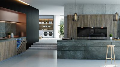 A luxurious, open-plan kitchen and laundry room featuring integrated Siemens appliances, including a dishwasher, oven, coffee machine, microwave, and stacked washer and dryer.