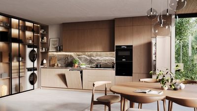 Cucina moderna con mobili in legno, paraschizzi in marmo, elettrodomestici da incasso, tavolo da pranzo rotondo, lampade a sospensione e una grande finestra con verde all'esterno.