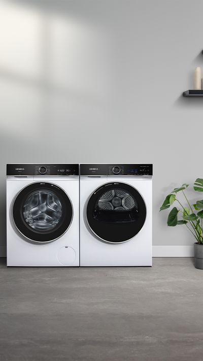 A modern laundry area featuring a washing machine and dryer, with a plant beside them, and clothes hanging in a closet.