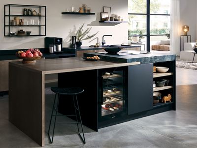 A modern open-plan kitchen and living area featuring a dark grey Siemens refrigerator, a kitchen island with a wine cooler, and contemporary decor.
