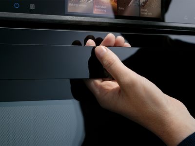 A hand opening the handle of a black oven, with the digital control panel visible above.