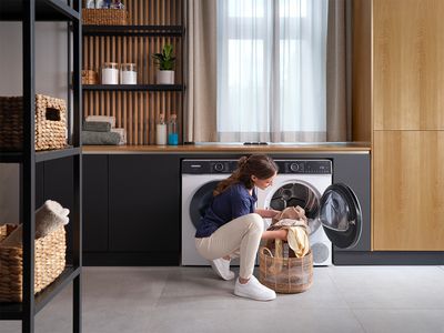A woman is loading clothes into a front-loading washing machine in a bright laundry room.  