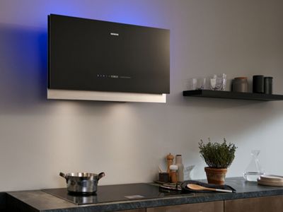 A black Siemens extractor hood with blue ambient lighting above an induction hob in a modern kitchen.
