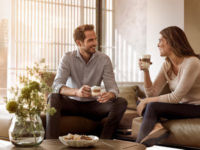 A smiling couple enjoying coffee and conversation on a sofa in a bright living room.