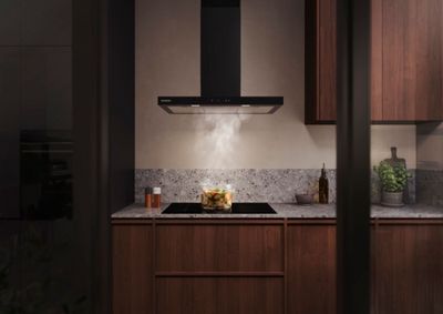 Moderne keuken met een glazen pan met stomende groenten op een inductiekookplaat onder een ge&iuml;ntegreerde blokschouwkap van Siemens.