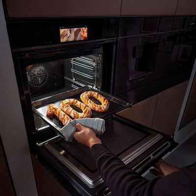 Una persona saca del horno moderno una bandeja con pretzels reci&eacute;n horneados, mostrando un interior de cocina elegante.
