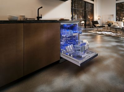 An open dishwasher with a blue interior light, filled with dishes, in a modern kitchen.