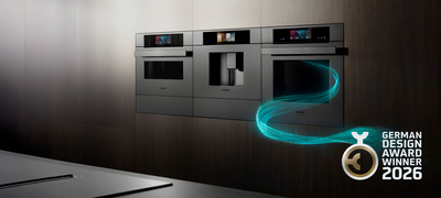 Elegante schwarze Siemens Ger&auml;te sind in eine dunkle strukturierte Wand in dieser modernen K&uuml;che integriert, erg&auml;nzt durch ein leuchtendes Designelement.     