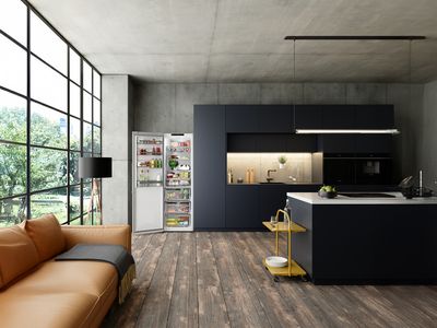 
       Une cuisine moderne avec un r&eacute;frig&eacute;rateur ouvert rempli de nourriture, une lampe &eacute;l&eacute;gante et des armoires &eacute;pur&eacute;es, le tout devant une grande fen&ecirc;tre lumineuse.
      