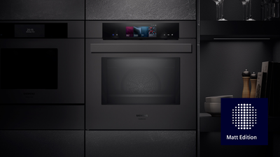 Ein eleganter schwarzer Siemens Ofen mit einem digitalen Steuerfeld &uuml;ber seiner Glast&uuml;r, nahtlos integriert in eine moderne schwarze K&uuml;che mit klaren Linien und matter Oberfl&auml;che.