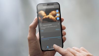 Una mano que sostiene un smartphone muestra una notificaci&oacute;n de una aplicaci&oacute;n sobre la finalizaci&oacute;n de un programa de dorado de alimentos, en el que aparecen croissants.